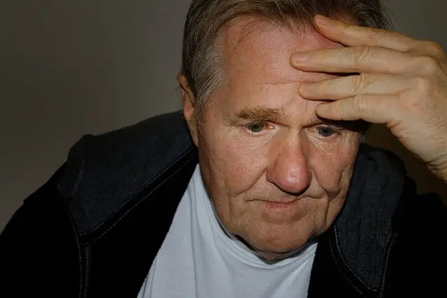 Elderly man holding his head in thought, appearing reflective and overwhelmed and depressed