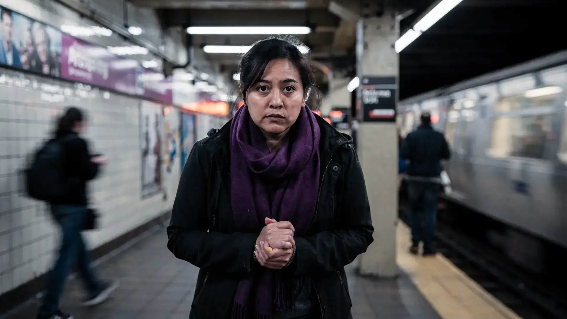 A New Yorker standing on a subway platform near Midtown, shoulders tense and hands clasped, with a subtle sense of overwhelm and vigilance. The mood communicates Signs Your Anxiety Might Be Something More without showing a panic scene.