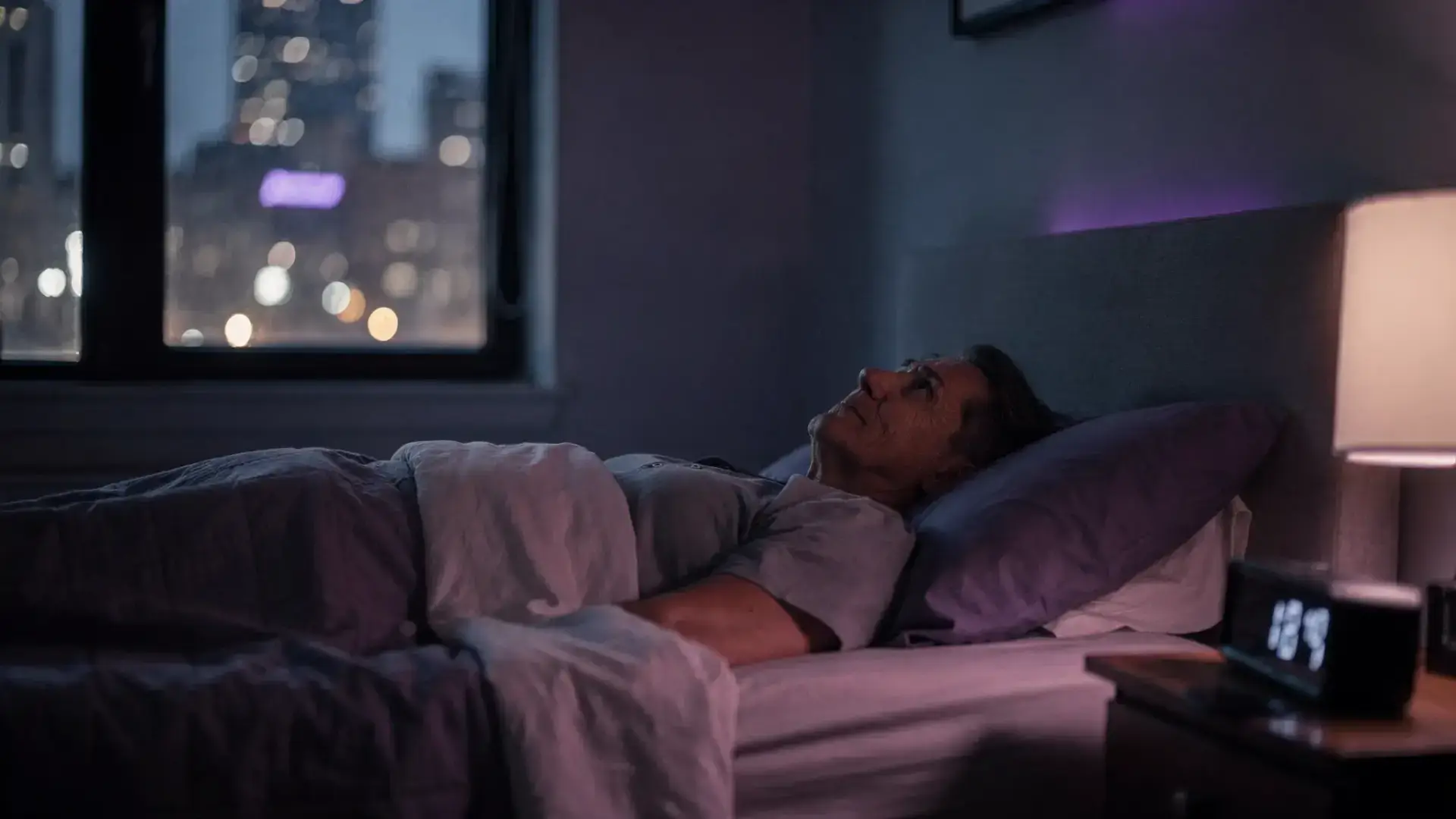 When Mood and Sleep Begin to Change in Midlife, a New York City professional lies awake at night in a dim bedroom, city lights visible through the window, conveying worry, fatigue, and racing thoughts.